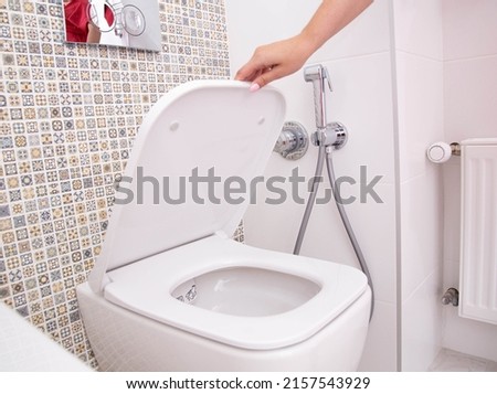 A woman's hand holds the toilet lid in the toilet. The concept of cleanliness and hygiene in the bathroom, pleasant smell of freshness Royalty-Free Stock Photo #2157543929