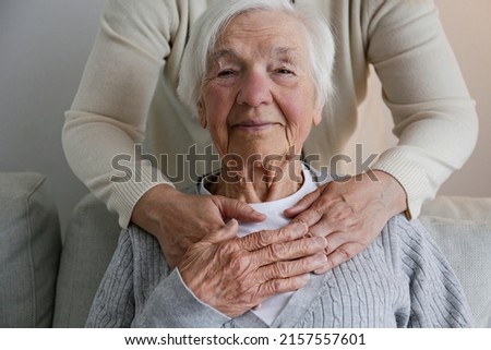 Unrecognizable female expressing care towards an elderly lady, hugging her from behind holding hands. Two adult women of different age. Family values concept. lose up, copy space, background. Royalty-Free Stock Photo #2157557601