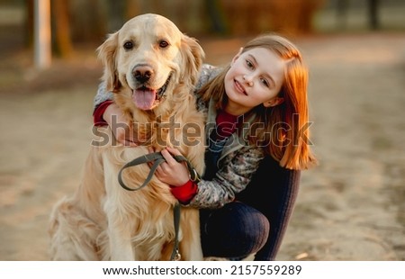 Preteen girl with golden retriever dog sitting in park in beautiful spring autumn day. Adorable female child kid hugging doggy pet outdoors and smiling portrait Royalty-Free Stock Photo #2157559289