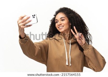 Happy carefree African-American young woman with curly hair taking selfie on the smartphone, recording video message, streaming in social medias, isolated on white