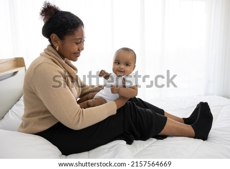 African young mother carrying and playing with her adorable baby on bed