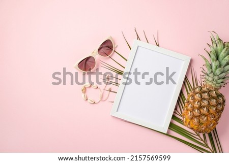 Summer vacation concept. Top view photo of white photo frame trendy sunglasses shell bracelet pineapple and palm leaves on isolated pastel pink background with copyspace