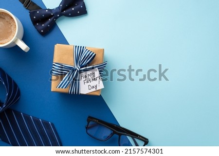 Father's Day concept. Top view photo of craft paper giftbox with ribbon bow and postcard cup of coffee glasses blue necktie and bow-tie on bicolor blue background with copyspace Royalty-Free Stock Photo #2157574301