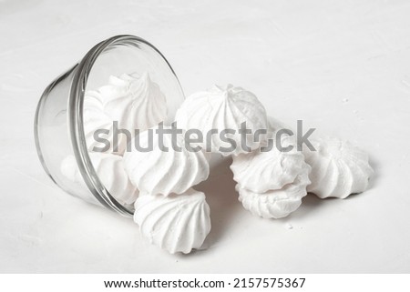 a glass vase with a French dessert meringue lies on a gray background, part of the meringue has spilled out of the vase onto the table. the vase in the picture is located with the back part.