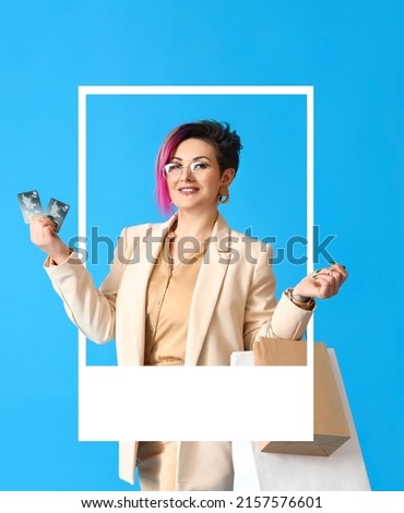 Beautiful woman with credit cards and shopping bags looking out of frame on blue background