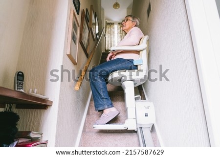 Senior woman using automatic stair lift on a staircase at her home. Medical Stairlift for disabled people and elderly people in the home. Selective focus Royalty-Free Stock Photo #2157587629