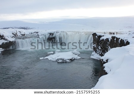 A group of tourists taking pictures near the edge of the famous Goðafoss (Godafoss) waterfall surrounded by ice and snow during winter in the north of Iceland, Europe