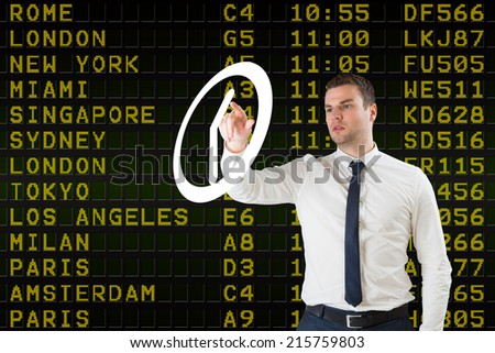 Young serious businessman pointing to a white clock against black airport departures board with yellow text