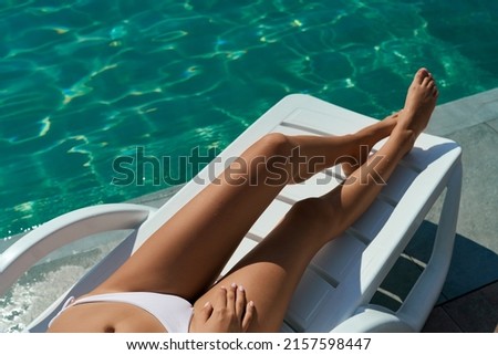 Close up of slim female lying on sunned near swimming pool. Seductive girl wearing white swimsuit sunbathing, having rest, relaxing outdoors. Concept of summertime and vacation.