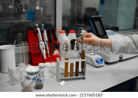 A hand in a biological laboratory worker places a test tube with a chemical sample into a test tube rack. 