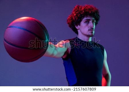 To challenge. Portrait of young muscular basketball player looking at camera isolated on purple background in neon. Concept of sport, movement, energy and dynamic, healthy lifestyle. Copy space for ad