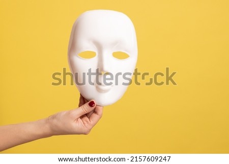 Profile side view closeup of woman hand holding white facial mask model, hiding personality. Indoor studio shot isolated on yellow background. Royalty-Free Stock Photo #2157609247