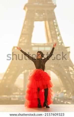 A vertical shot of a Black young female in front of the Eiffel Tower