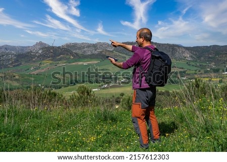 man with backpack man orienting himself in the mountains with his mobile phone, mountain landscape in the background and cloudy sky