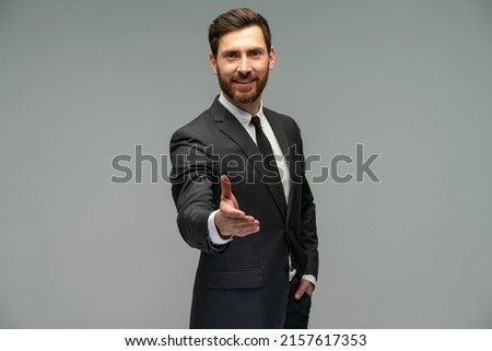 Male businessman in a suit stretching hand and shows a palm up gesture on a grey background. Concept of request, handshake 