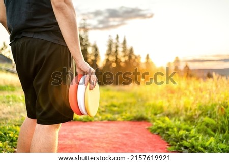 Disc golf in summer at sunset. Man with equipment in park course. Guy playing discgolf. Player in outdoor sport tournament. Landscape in Finland.