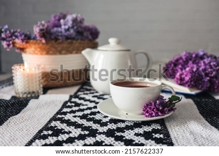 A cup of tea with a teapot on a table with a lilac wicker basket, atmospheric tea party photo.