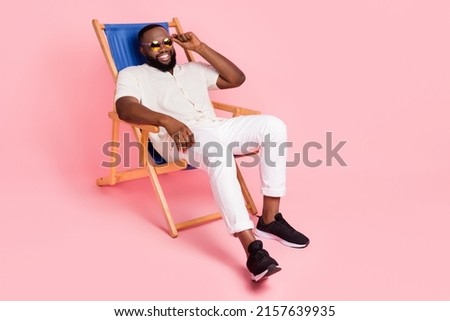 Full size photo of satisfied cheerful man sitting chaise lounge touch glasses isolated on pink color background