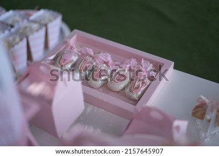 White heron-shaped cookies with a pink bow on the wooden stick of the ice cream and a rainbow drawn on the front decorating a pink square tray of a girl's sweet table.