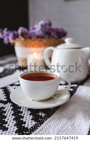 Cup of tea and branches of blooming lilac on wooden table.