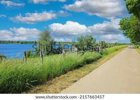 Beautiful scenic rural dutch landscape , river Maas lake, straight cycling path, green trees, blue sky cumulus clouds - Ohe en Laak, Netherlands Royalty-Free Stock Photo #2157663457
