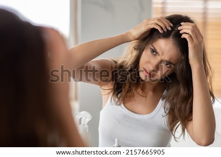 Unhappy Lady Searching Hair Flakes Having Dandruff Problem Looking At Mirror Standing In Bathroom At Home. Hair Loss And Lice Treatment. Haircare And Head Skin Health Concept. Selective Focus