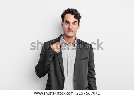 young businessman looking happy, proud and surprised, cheerfully pointing to self, feeling confident and lofty