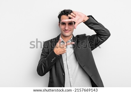 young businessman feeling happy, friendly and positive, smiling and making a portrait or photo frame with hands