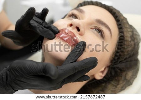 Cosmetologist applies an analgesic cream to the lips and covers it with a transparent film, stretch. Royalty-Free Stock Photo #2157672487