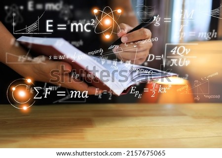 Physics equations floating in the background, hands writing in notebooks on wooden tables, representing the learning teaching or scientific notes of Albert Einstein and Sir Isaac Newton or physics all Royalty-Free Stock Photo #2157675065