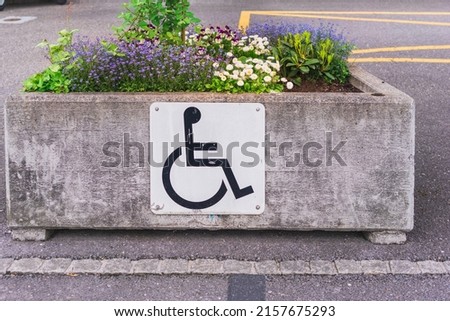 Disabled parking sign on a concrete box with blooming flowers in an open street parking lot in Liechtenstein's capital Vaduz, caring for people with disabilities