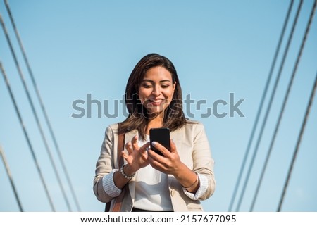 A happy elegant young woman stands and uses her phone to type an important message. A businesswoman using technologies outdoors. Royalty-Free Stock Photo #2157677095