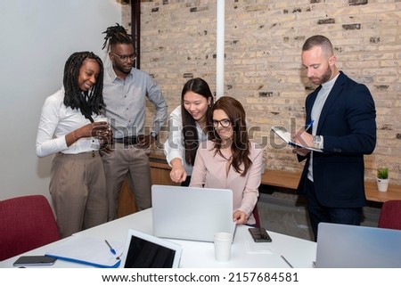 Young multi-ethnic business team working on a project, sharing ideas and analyzing data around a colleague sitting at the table looking at the computer in an office