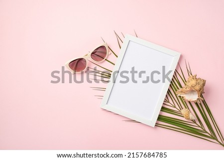 Summer rest concept. Top view photo of white photo frame trendy sunglasses shells and palm leaves on isolated pastel pink background with copyspace