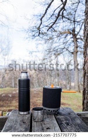 A set of tourist dishes for quick cooking, a black pan for porridge on a hike, a vacuum thermos for tea, a steel mug. High quality photo