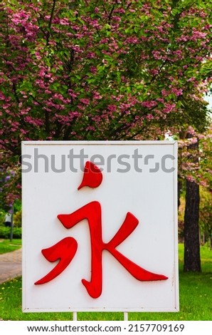 The Japanese hieroglyph for meaning-Eternity. White plate with red Japanese hieroglyph for meaning-eternity. Blurred blooming sakura trees in the background.