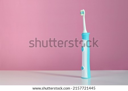 Electric toothbrush with replaceable nozzles on a white table, pink background. Dental care