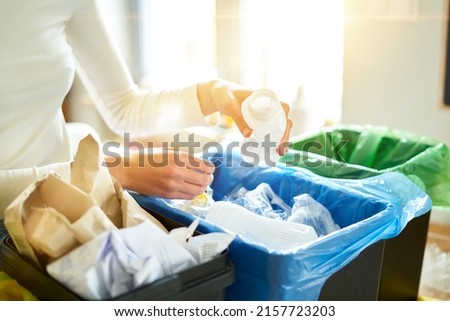 Woman putting empty plastic bottle in recycling bin in the kitchen. Person in the house kitchen separating waste. Different trash can with colorful garbage bags. Royalty-Free Stock Photo #2157723203