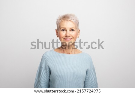 Elderly beautiful woman with a short pixie haircut in a blue sweater on a gray background Royalty-Free Stock Photo #2157724975