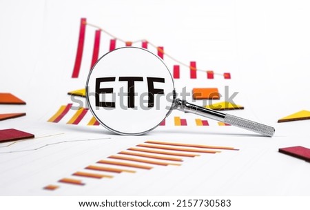 Exchange traded fund. Magnifying glass with ETF text and graphs showing stock market fall. Analysis of economic recession and crisis, risks from shares purchase or sale. High quality photo