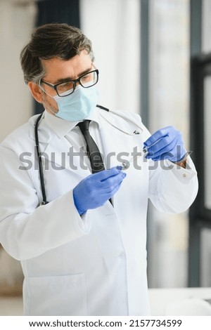 Mid aged male doctor wearing protective mask holding a syringe with vaccine