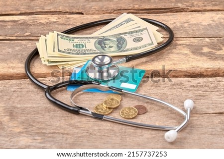 Stethoscope money, coins and credit cards concept. Wooden desk background.
