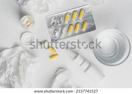 Glass of water, nasal spray, pills in blister and used paper tissue on table. Flu treatment concept