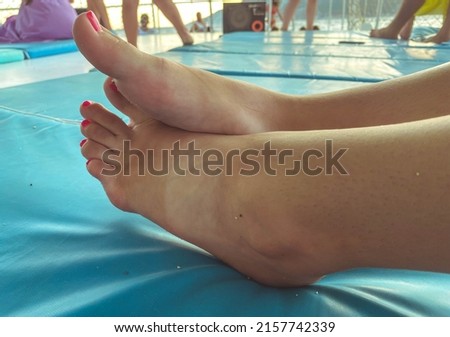 female legs with a pedicure lie on a beach lounger with a mattress. the girl's nails are painted in pink trendy color. foot care, pedicure for decoration.