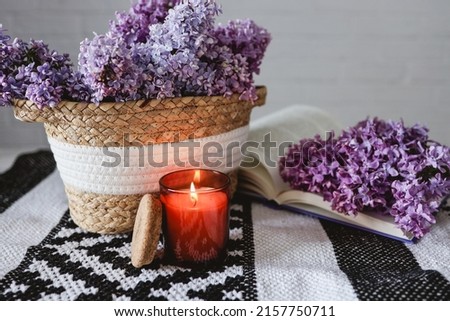 Wicker basket with lilacs, a candle, an open book on the table.Good morning concept.
