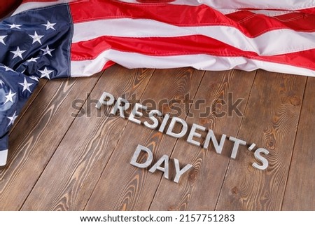 words presitdents day laid with silver metal letters on wooden surface near crumpled US flag