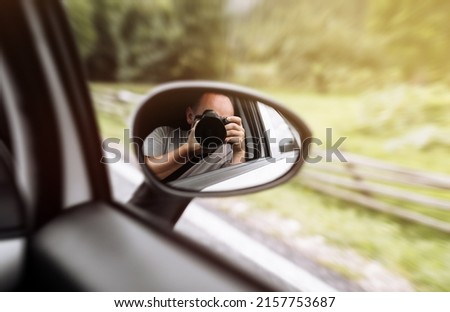 man takes photo in mirror in car. A man is taking photo someone or something from an open car window. Reflection in the side mirror of the car.