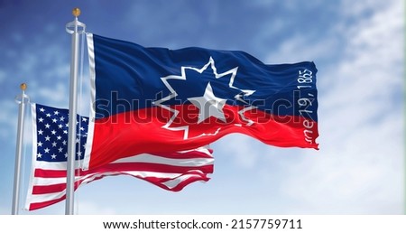 The Juneteenth flag waving in the wind with the american flag. Juneteenth is a federal holiday in the United States commemorating the emancipation of enslaved African-Americans Royalty-Free Stock Photo #2157759711