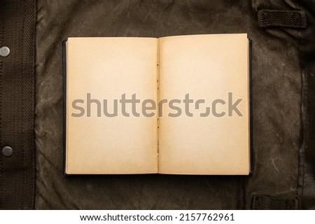 An open book with yellowed pages on an old backpack. Vintage khaki canvas background.