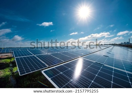 Solar panes in a solar park used for clean energy production. Solar panel under blue sky with sun. Green grass and cloudy sky. Alternative energy concept to reduce global warming and climate change Royalty-Free Stock Photo #2157795255